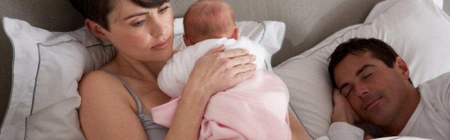 Mother Cuddling Newborn Baby In Bed At Home